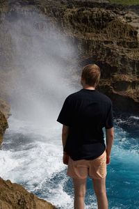 Rear view of man looking at splashing water in sea