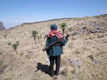 Rear view of man with rifle standing on field