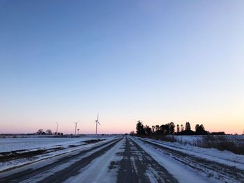 Snow covered road against clear sky during sunset