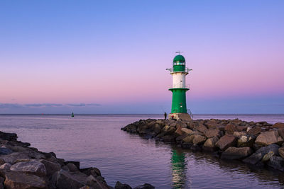 Lighthouse by sea against sky during sunset