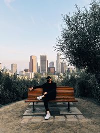 Man sitting on bench against buildings in city