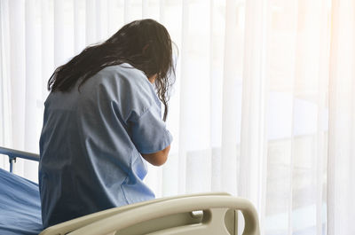 Rear view of woman standing by window at home