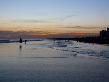 Silhouette people on beach against sky during sunset