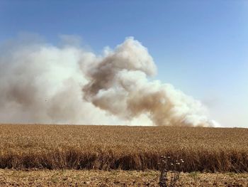 Smoke emitting from chimney on field against sky