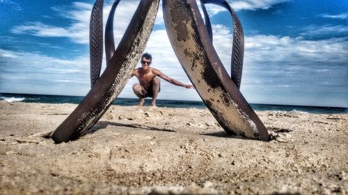 Full length of shirtless man jumping on beach against sky