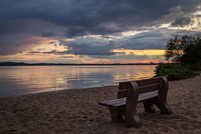 Empty chairs on beach against sky during sunset