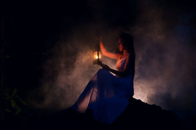 Woman holding lit candle against sky at night