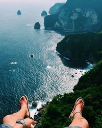 Low section of man sitting on cliff against sea