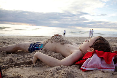 Boy lying on sand at beach against sky