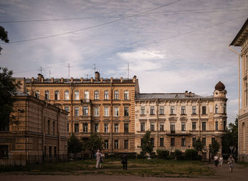 People walking by buildings in city against sky