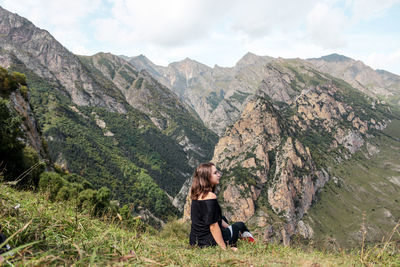 Side view of young woman sitting against mountain range