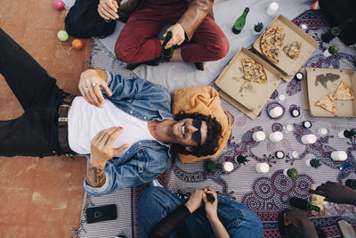 Directly above shot of happy man lying down on blanket by friends in party at rooftop