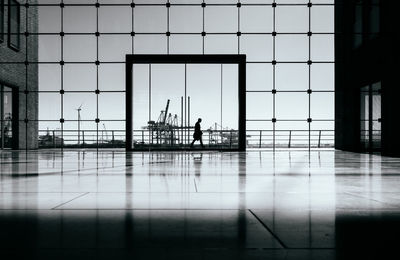 Silhouette of man walking behind modern glass building in front of harbour scene