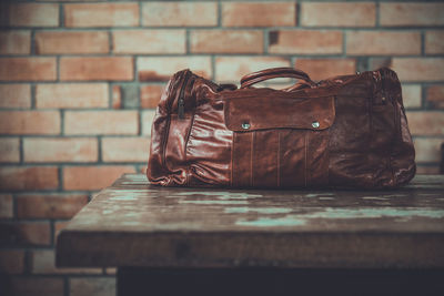 Close-up of leather bag on table against brick wall