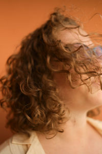 Wind blows curly hair. caucasian white girl on orange background. selective focus. close-up.