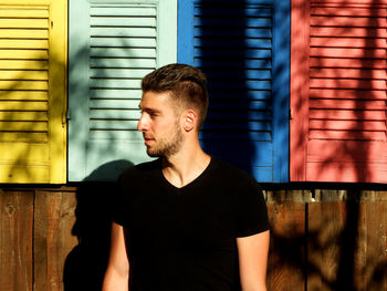 Young man looking away while standing against wall