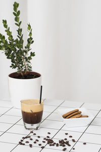 Coffee and biscuits by potted plant on floor against white wall