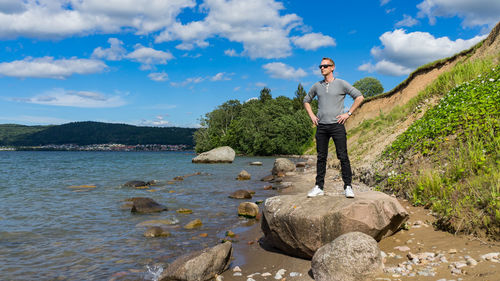 Mid adult man with hand on hip standing on rock at beach