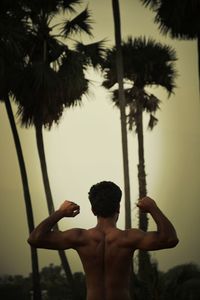 Rear view of shirtless man standing by palm trees