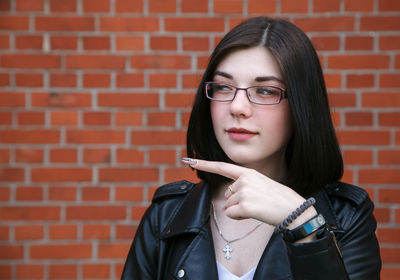 Portrait of young woman standing against brick wall