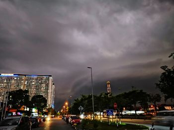 Cars on city street against cloudy sky