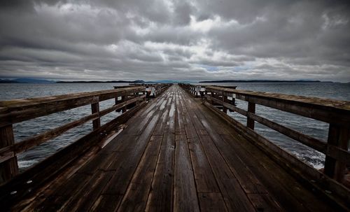 Pier over sea against storm clouds