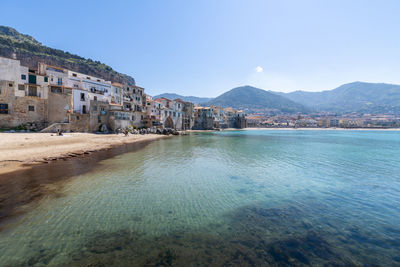 Buildings by sea against clear blue sky