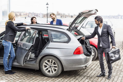 Colleagues discussing while businessman unloading bags from car
