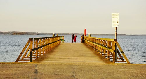 Friends standing on pier by sea against clear sky