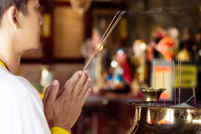 Side view of young man holding incense while praying in temple