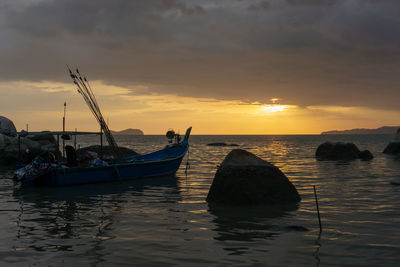 Sailboats moored in sea against sky during sunset