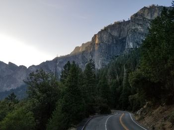 Road amidst trees and mountains against sky