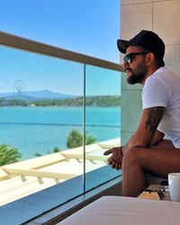 Side view of man looking at sea while sitting in balcony