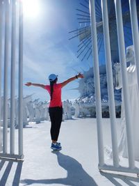 Woman with arms outstretched standing on snowy field against sky