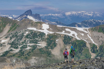 Rear view of hikers standing at mountains against sky during winter