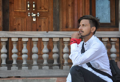 Side view of a young guy looking ahead while sitting on temple stairs posing with hand on chin