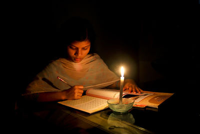 Midsection of man holding lit candles in darkroom