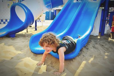 Full length of cheerful boy lying on slide at playground