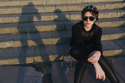 Portrait of young man wearing sunglasses while sitting on footpath