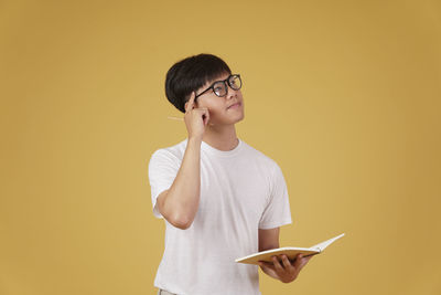 Young man looking away while standing against yellow background