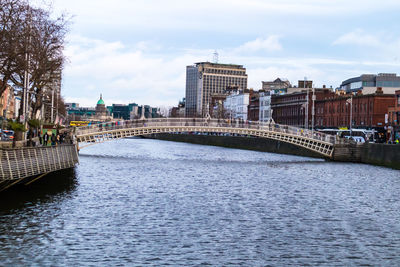 Bridge over river by buildings against sky in city