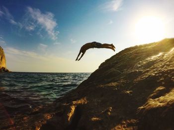 Man jumping on rock in sea against sky