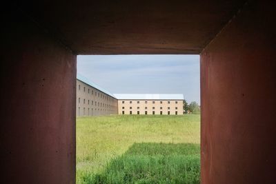 Buildings on field against sky seen through window