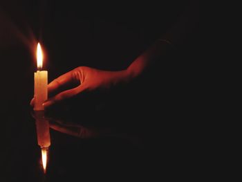 Close-up of hand holding lit candle in darkroom