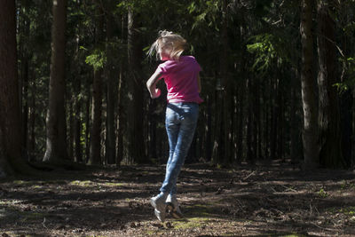 Full length of girl jumping in forest against trees