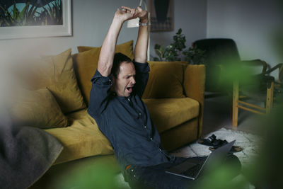 Businessman stretching hands while sitting with laptop in living room