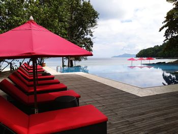 Lounge chairs by swimming pool at beach against sky