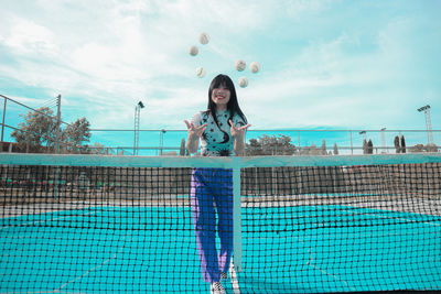 Portrait of young woman standing by swimming pool against sky