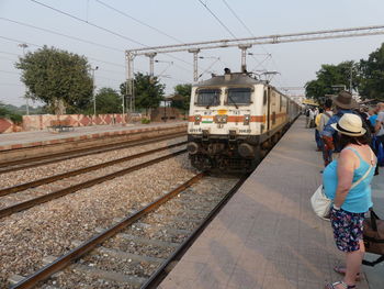 Rear view of people on railroad tracks against sky