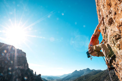 Low angle view of man rock climbing against blue sky during sunny day